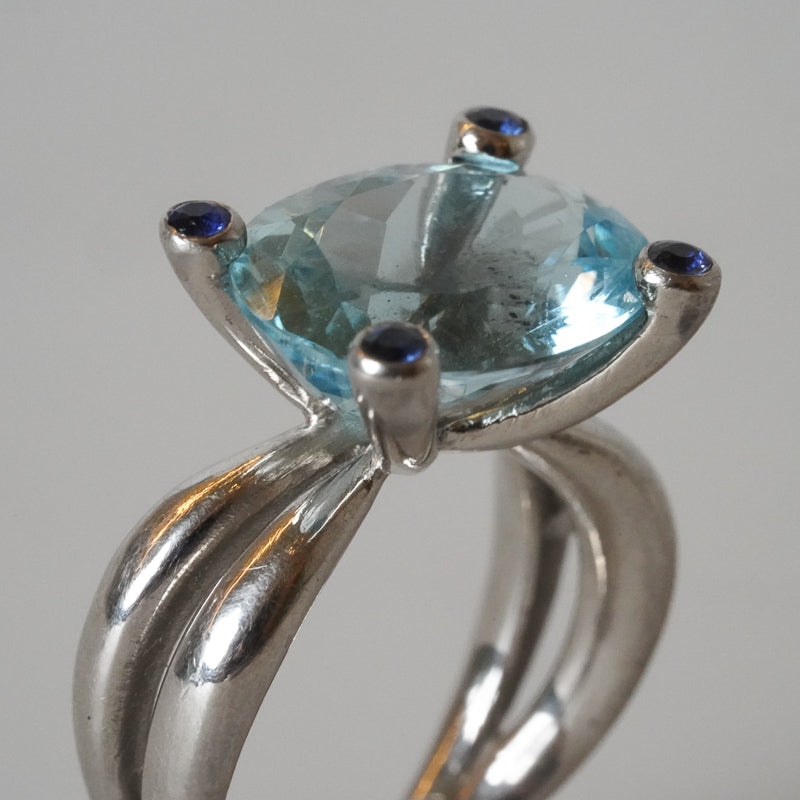 A platinum ring with a large aquamarine gemstone and blue sapphires, designed by Gudrun Hillmann  front view